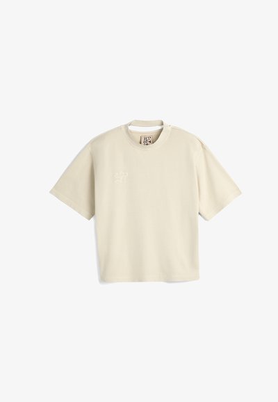 Cremefarvet kortærmet t-shirt i blødt stof, med en subtil broderet design på venstre bryst og rund halsudskæring.