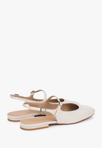Jasno beżowe buty typu slingback z gładką skórzaną teksturą, spiczastym noskiem i małym, drewnianym obcasem, wyposażone w regulowany pasek na kostkę.