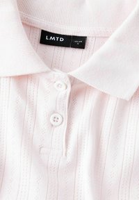 Polo shirt rose clair avec des rayures verticales, en tissu texturé, doté d'un plastron à trois boutons et d'un col doux. Étiquette de marque visible.