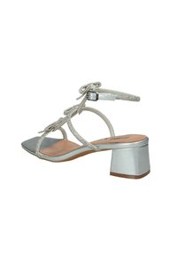 Sandali con tacco quadrato argentati, con fasce decorate e un tacco a blocco. Presentano un delicato cinturino alla caviglia con un dettaglio a fiocco.