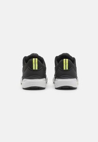 Black athletic shoes with a textured upper, white midsole, rubber outsole, and distinctive yellow stripes on the heel for visibility.