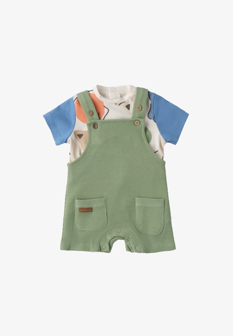 Grüner kariertes Overall mit Holzknöpfen, der zwei Vordertaschen hat. Darunter ein kurzärmliges Shirt mit bunten abstrakten Formen.