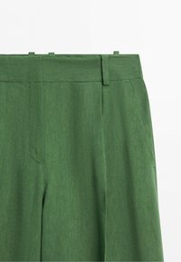 Groene hoge taille broek met riemlussen en zijzakken, gemaakt van gestructureerde stof, getoond tegen een effen witte achtergrond.