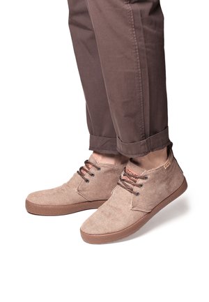 Baskets en toile brunes avec une tige texturée, des lacets marron et des semelles en caoutchouc. Les chaussures présentent un bout arrondi et un léger talon.