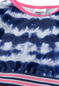 Haut de maillot de bain bleu marine avec un motif tie-dye dans des nuances de blanc. Présente une bordure rose autour de l'encolure et une bande rayée en bas.