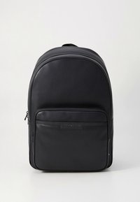 Black leather backpack with a smooth texture, rounded top, front zip pocket, and brand logo on the front panel. Sturdy design with adjustable straps.