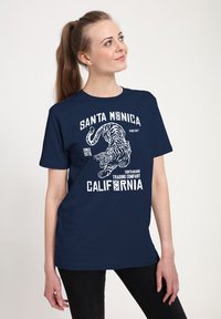 Námořnická modrá tričko s grafickým designem, který zobrazuje bílého tygra, text "Santa Monica" a "California", s uvolněným střihem a jemnou látkou.
