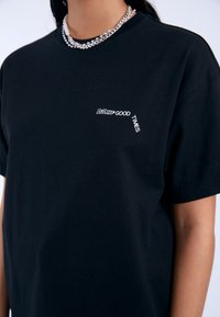 Camiseta de algodón negra con un pequeño gráfico blanco que dice "BUENOS MOMENTOS" en la parte superior izquierda, con una textura suave y un corte relajado.