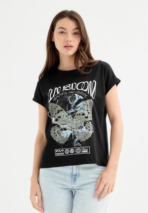 Camiseta de algodón negra de manga corta con un gráfico de mariposa y texto. Corte relajado con mangas enrolladas, sobre un fondo claro.