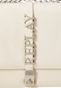 Beige Lederhandtasche mit einem silbernen Kettenriemen, rechteckiger Form und geprägtem "REPLAY"-Schriftzug auf der Vorderklappe.