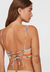 Multi-kleurige bikinibovenstuk met dunne bandjes, voorzien van een crisscross rugontwerp en een striksluiting, gemaakt van rekbaar materiaal.