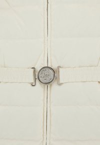 Giacca imbottita color crema con chiusura a zip, dotata di una larga cintura elasticizzata e una fibbia circolare metallica in vita.