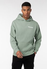 Hellgrüner Hoodie aus weichem Stoff. Mit einer Kängurutasche und gerippten Bündchen. "WORLDWIDE"-Logo in Weiß über der Brust.