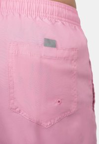 Pantaloni shorts rosa realizzati in tessuto leggero con una cintura elastica. Presentano una tasca posteriore con un'etichetta grigia e dettagli di cucitura visibili.