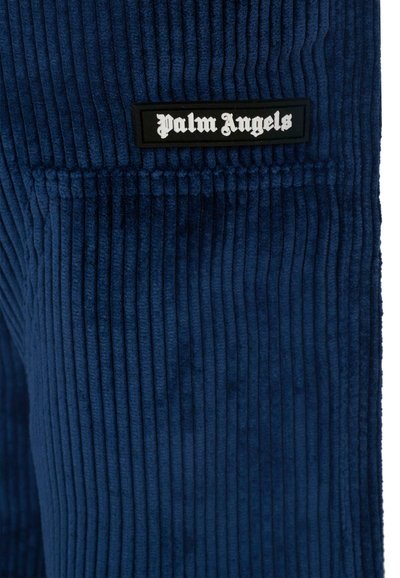 Navy corduroy stof met verticale ribbels. Heeft een zwart label met "Palm Angels" in witte gotische lettertype. Zachte textuur en gestructureerd ontwerp.