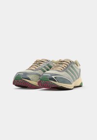 Un paio di scarpe da corsa grigie e verdi con lacci beige e suole testurizzate con punta rosa, mostrate da un angolo anteriore basso.