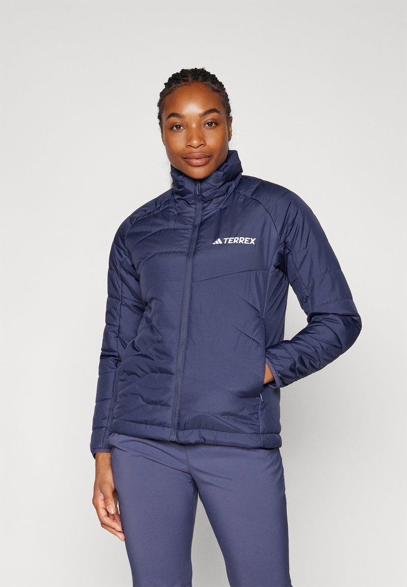 Veste isolante marine avec un col haut, fermeture éclair et logo Terrex. Présente un motif matelassé et des poches latérales.