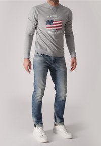 Šedá dlouhá mikina s potiskem vlajky Spojených států na přední straně, v kombinaci s světle modrými džíny a bílými teniskami. Volný a pohodlný styl.