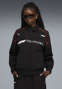 Black bomber jacket with red accents, featuring a Formula 1 logo and Puma branding. Smooth texture with ribbed cuffs; paired with matching pants.