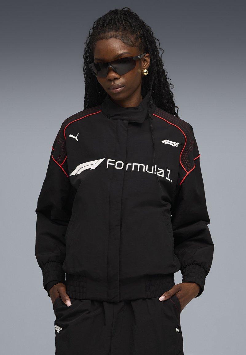 Black bomber jacket with red accents, featuring a Formula 1 logo and Puma branding. Smooth texture with ribbed cuffs; paired with matching pants.