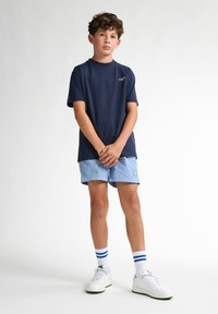 Marinblå bomull t-shirt med en grön logotyp, i kombination med ljusblå shorts och vita sneakers med gröna detaljer samt blå-randiga strumpor.