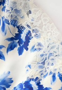 Bloemenpatroon stof in tinten blauw op een witte achtergrond,accentueert met delicate witte kant trim en rafelige randen.