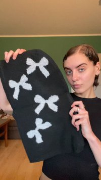 Black scarf with white textured bows displayed prominently. Knit material with a soft surface and a rectangular shape.