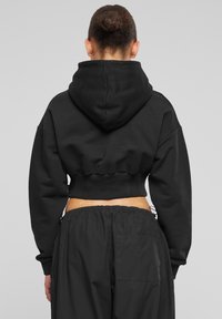 Avskuren svart hoodie med en rymlig huood, lösa ärmar och ribbad nederkant. Kombinerad med svarta byxor med resårmidja och ficka.