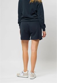 Shorts en coton bleu marine avec une coupe décontractée, présentant une texture lisse et des poches latérales, associés à des baskets légères et un sweat-shirt sombre assorti.