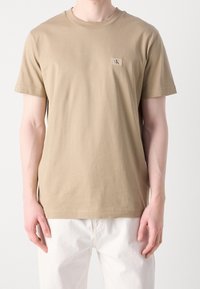 Tan bomulls t-shirt med rund hals och korta ärmar. Har en liten logotyp på bröstet och en avslappnad passform.