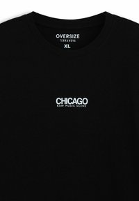 T-Shirt oversize nera in cotone, con scollo rotondo. Testo bianco che recita "CHICAGO RAW MUSIC SCENE" sul fronte.