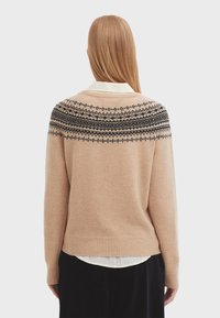 Beige gestrickter Pullover mit einem schwarzen Fair-Isle-Muster an der Passe. Leichter Stoff, runder Ausschnitt, gerippter Saum und Bündchen.