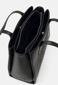 Czarna skórzana torba tote z dwoma przegrodami, srebrnym zamkiem błyskawicznym i wytłoczonym logo. Posiada podwójne uchwyty i usztywniony kształt.