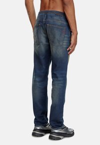 Jean en denim bleu pour homme avec une coupe décontractée, une taille élastique, cinq poches et des détails légèrement décolorés. Quincaillerie en argent et accents de couture.