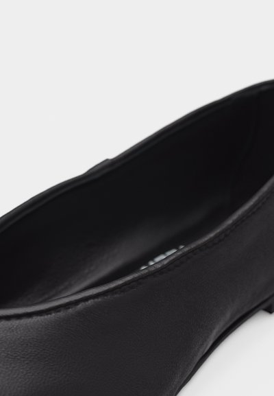 Κοντινή λήψη ενός μαύρου δερμάτινου παντόφλας με επίπεδη σόλα που δείχνει ομαλή υφή και ραφές κατά μήκος της πάνω άκρης.