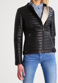 Černá prošívaná kožená bunda se zipovým zapínáním, postranními kapsami a kontrastním béžovým podšívkou. Má fitted design a dekorativní kování.