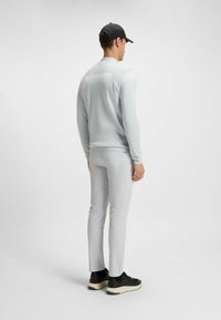 Maglietta a maniche lunghe grigio chiaro con retro testurizzato, abbinata a pantaloni aderenti grigio chiaro e scarpe da ginnastica nere con suola crema.