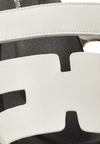 Sandalía de cuero blanco con correas anchas, diseño recortado y suela negra texturizada. Destacada por su forma geométrica y estilo minimalista.
