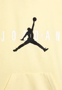 Sudadera amarilla con un gráfico negro de una figura saltando y el texto blanco "J O R D A N" debajo. Textura suave con bolsillo tipo canguro.