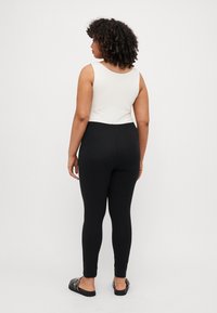Zwarte legging met een slim fit en rekbare stof, gecombineerd met een witte mouwloze top met een ronde hals. Zwarte instappers.