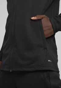 Veste de sport noire en tissu texturé, avec fermeture �éclair, poches latérales et marquée du logo "DRYCELL" sur l'ourlet.