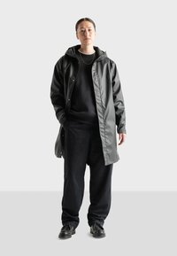 Black waterproof raincoat with a hood, snap buttons, and front pockets, paired with a black sweatshirt and pants. Worn with black shoes.