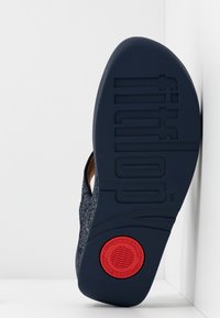 FitFlop-sandal med en teksturert marineblå overdel, beige aksenter og en gummisåle med en rød sirkulær logo og riller for grep.