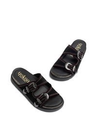 Sandali in suede nero con tre cinturini regolabili dotati di fibbie metalliche e cuciture rosse, presentano un plantare imbottito e una suola testurizzata.