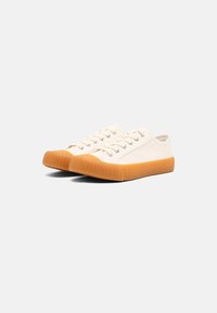 Canvas sneakers in off-white with a rubber, ribbed orange sole. Features metal eyelets and flat cotton laces. Low-profile design.