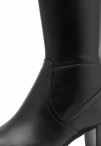 Botte en cuir noir à hauteur de genou avec une texture lisse, une tige droite, des détails de couture subtils et un talon carré.
