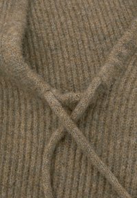 Strickpullover in einem hellbraunen Farbton mit gerippter Textur, der mit einem verdrehten Bindebandverschluss am Hals für zusätzliche Details ausgestattet ist.