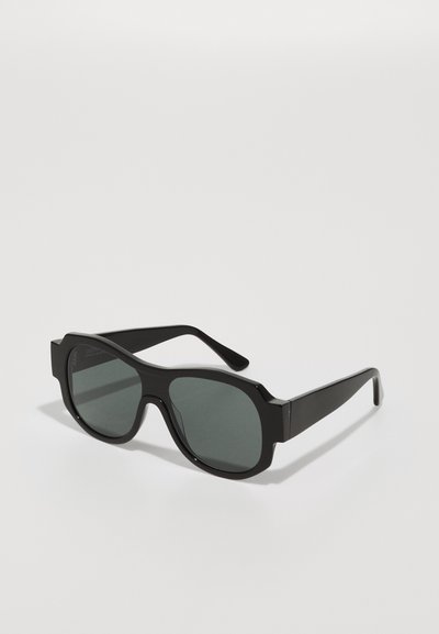 Occhiali da sole neri con montatura rettangolare e oversize. Lenti scure, texture liscia e accenti leggermente sollevati sul bordo superiore della montatura.