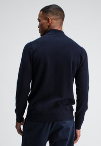 Dunkelblauer Strickpullover mit hohem Kragen und gerippten Bündchen. Weiche Textur, taillierte Passform, mit glattem Rücken ohne Muster.