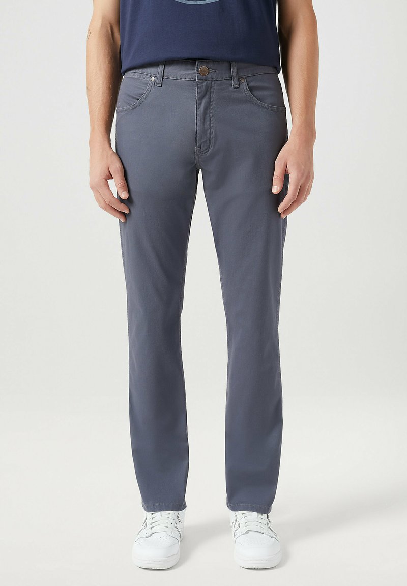 Grijze katoenen broek met een rechte snit, voorzien van voorzakken en een knoopsluiting in de taille, gecombineerd met witte sneakers.